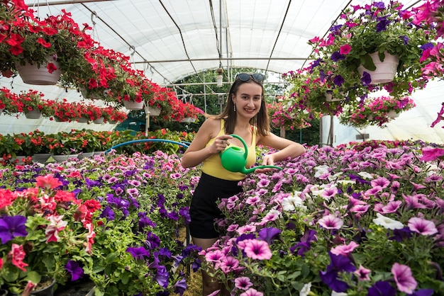 Porträt des schönen Gärtners der Frau, der Pflanzen und Blumen im Gewächshaus wässert