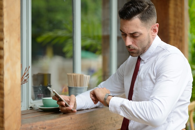 Porträt des schönen Geschäftsmannes mit Stoppelbart, der am Kaffeehaus draußen entspannt