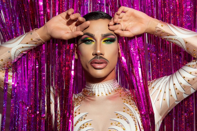 Foto porträt des schönen jungen mannes in drag queen make-up, der die kamera und den bunten hintergrund betrachtet