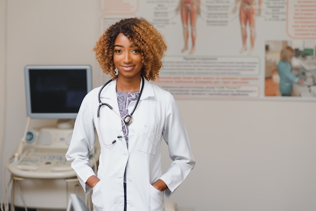 Porträt des schönen lächelnden weiblichen Afroamerikanerarztes, der in der Arztpraxis steht