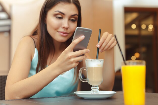 Porträt des schönen Mädchens, das ihren Handy im Café verwendet