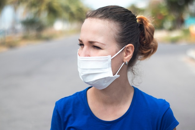 Porträt des schönen Mädchens, der jungen Person, der Frau in der medizinischen sterilen Schutzmaske auf Gesicht, das allein an der leeren Straße draußen steht. Coronavirus, Pandemie, epidemisches Viruskonzept. Covid19 Quarantäne