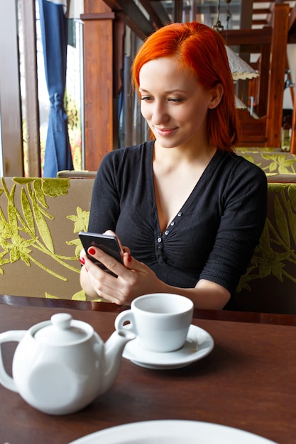 Porträt des schönen Mädchens im Hut unter Verwendung ihres Handys im Café. Tonned