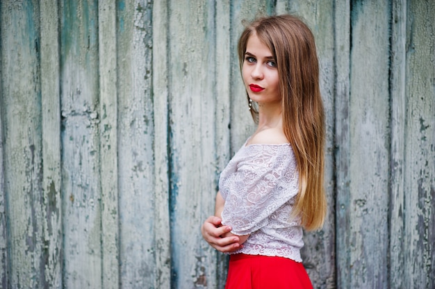 Porträt des schönen Mädchens mit den roten Lippen gegen hölzernen Hintergrund, Abnutzung auf rotem Kleid und weißer Bluse