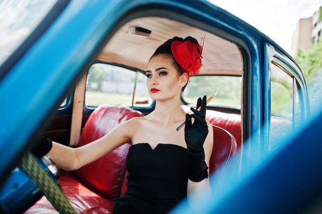 Porträt des schönen sexy Modemädchenmodells mit hellem Make-up im Retrostil, der in der Hand im Weinleseauto mit einer Zigarette sitzt.