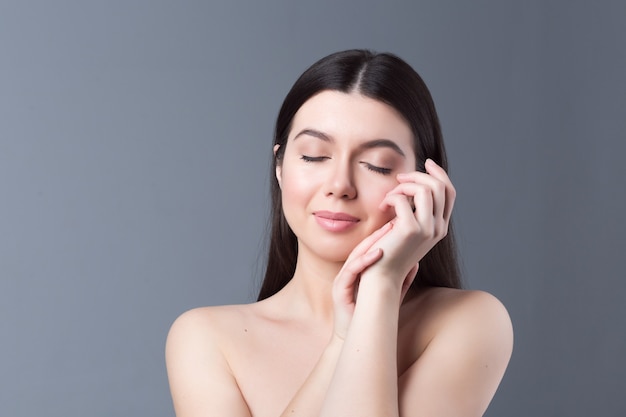 Porträt des Schönheitsmädchens mit natürlichem nacktem Make-up, das ihr Gesicht berührt. Wellness, Hautpflege