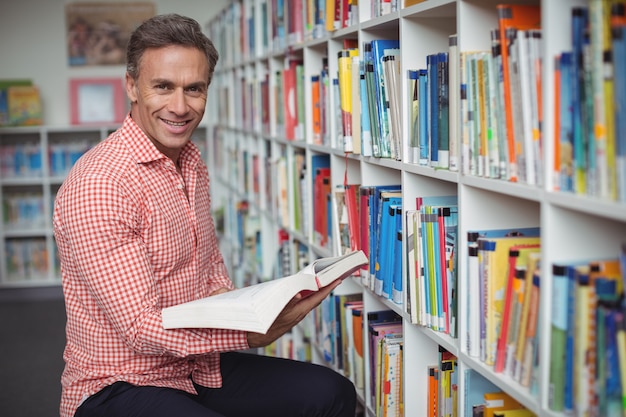 Porträt des Schullehrers, der Buch in der Bibliothek hält