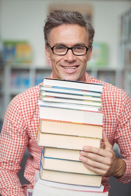 Porträt des Schullehrers, der Stapel Bücher in der Bibliothek hält