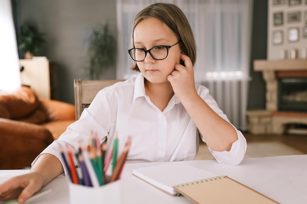 Porträt des Schulmädchens, das drinnen am Tisch sitzt und ihre Hausaufgaben macht Das Mädchen macht Hausaufgaben zu Hause Fernunterricht Lektionen Hausaufgabenerziehung