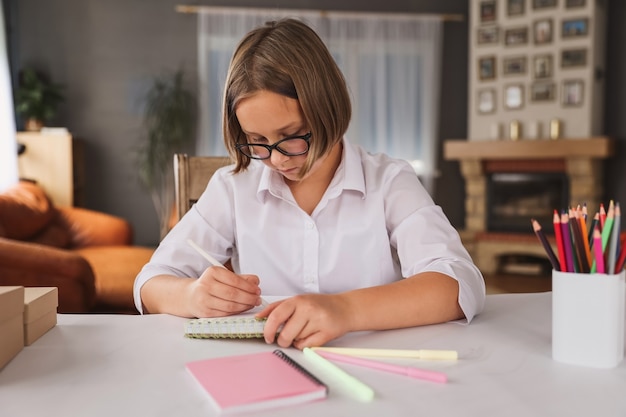 Porträt des Schulmädchens, das drinnen am Tisch sitzt und ihre Hausaufgaben macht. Das Mädchen macht Hausaufgaben zu Hause. Fernunterricht. Unterricht, Hausaufgaben, Bildung.