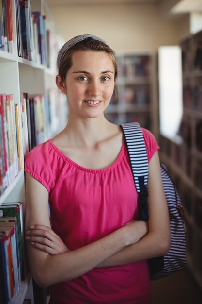 Porträt des Schulmädchens, das mit verschränkten Armen in der Bibliothek steht