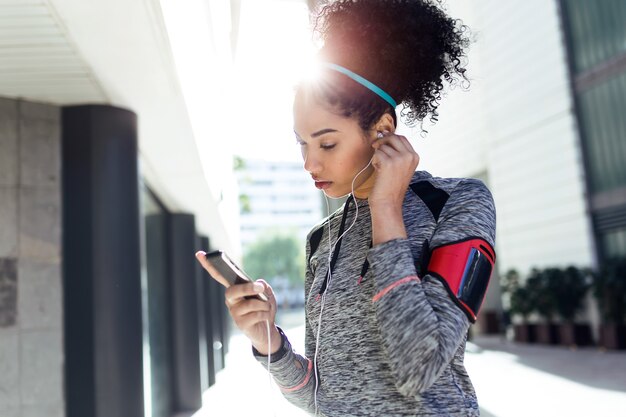 Porträt des Sitzes und der sportlichen jungen Frau, die Musik mit Handy hört.