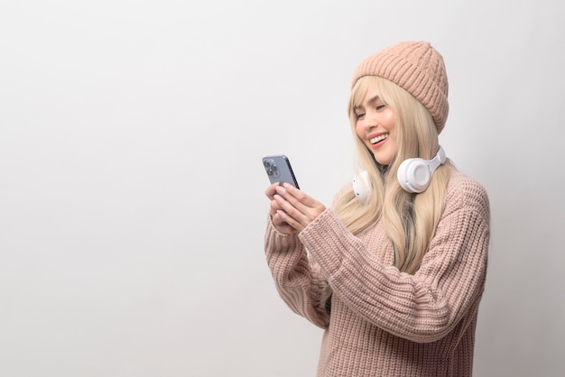 Porträt des tragenden Pullovers der kaukasischen jungen Frau, der intelligentes Telefon über weißem Hintergrund hält