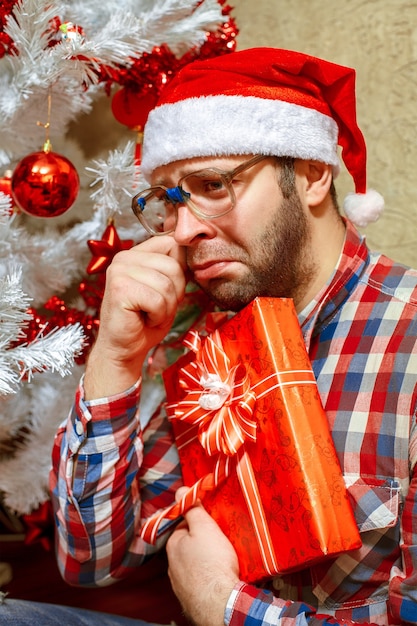 Porträt des traurigen Mannes mit Weihnachtsgeschenk in der Weihnachtsmütze