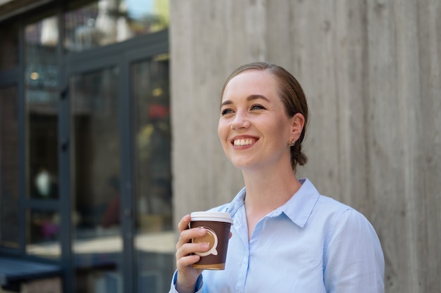 Porträt des trinkenden Kaffeestandes der glücklichen überzeugten jungen Geschäftsfrau in der Stadt im Freien. Foto in hoher Qualität