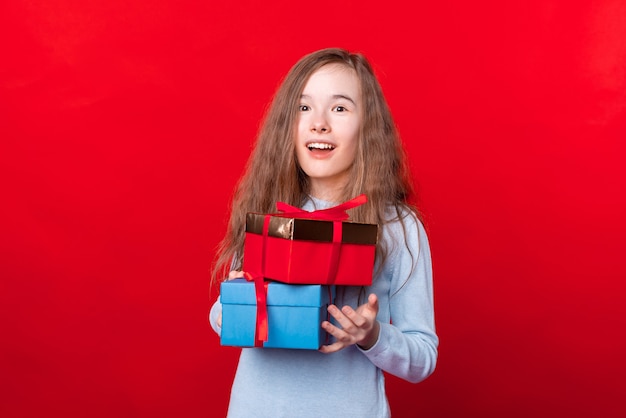 Porträt des überraschten kleinen Mädchens, das Geschenkboxen über roter Wand hält