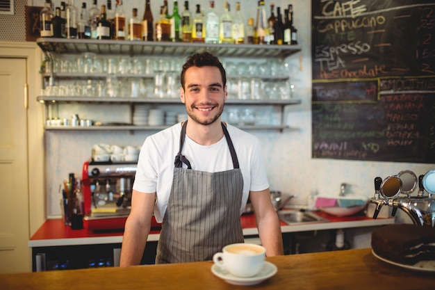 Porträt des überzeugten Kellners mit Kaffee am Zähler im Café