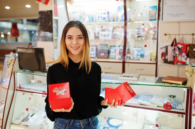 Porträt des verkäufers der jungen kaukasischen frau halten rote geschenkboxen. kleines geschäft von süßigkeiten souvenirs shop.