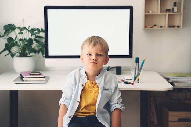 Porträt des Vorschulkindjungen auf dem Hintergrund des Computers mit leerem weißem Bildschirm im Wohngebäude Kinder online lernen Fernunterricht Entwicklung oder Unterhaltung Kids homeschooling