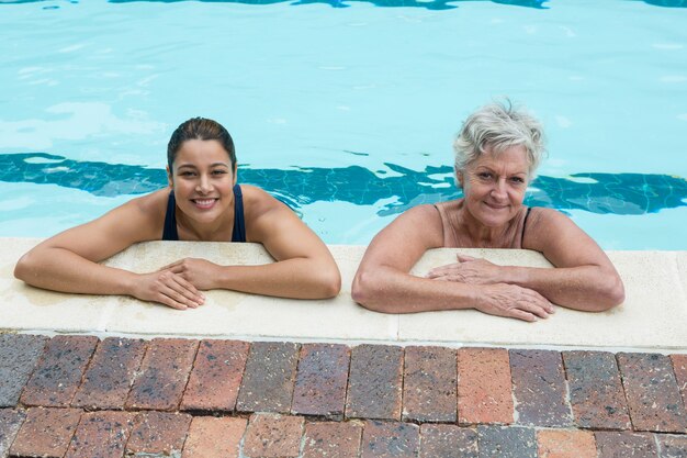 Porträt des weiblichen Trainers und der älteren Frau, die sich am Pool lehnen