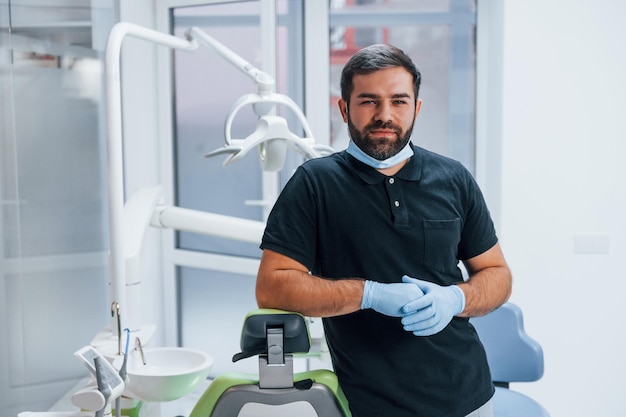 Porträt des Zahnarztes in Handschuhen, der drinnen in der Klinik steht.