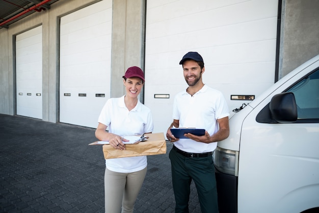 Porträt des Zustellers und der Frau, die mit Klemmbrett und Paket stehen