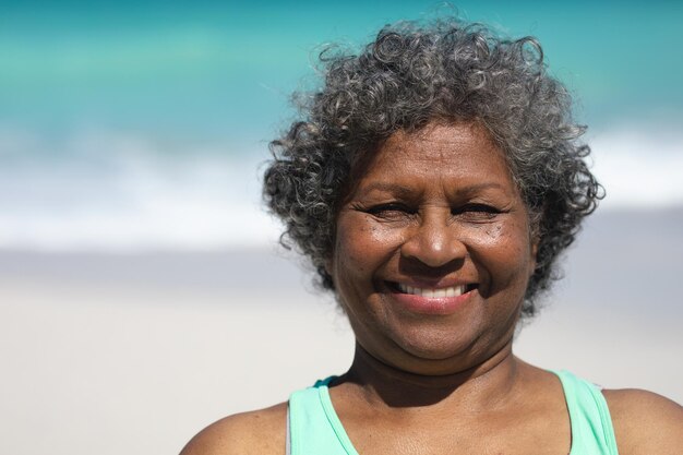 Porträt einer älteren afroamerikanischen Frau mit kurzen grauen lockigen Haaren auf einem Strand in der Sonne, die zur Kamera lächelt