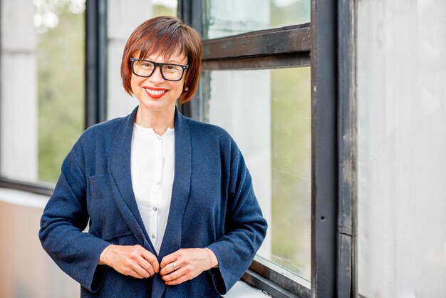 Porträt einer älteren eleganten Frau, die drinnen in der Nähe des Fensters steht