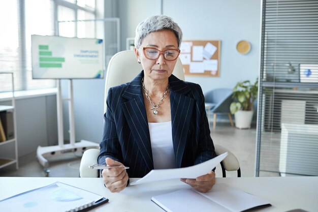Porträt einer älteren Frau als Chefin, die am Arbeitsplatz im Büro sitzt und ein Dokument liest