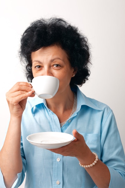 Porträt einer älteren Frau, die aus einer Tasse trinkt und eine Untertasse hält