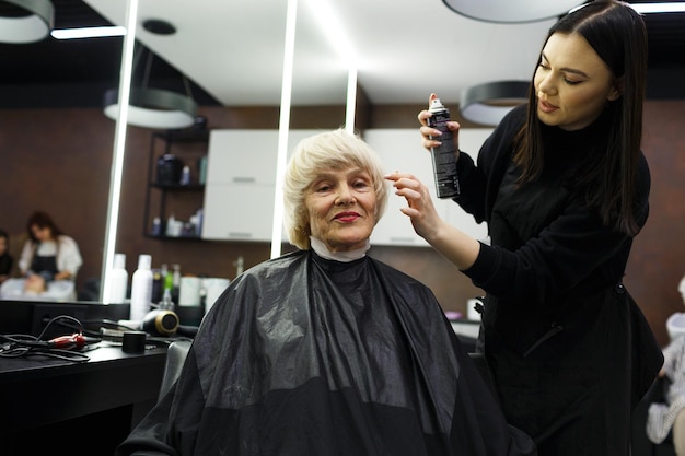 Porträt einer älteren Frau, die einen professionellen Friseur besucht. Ein erfahrener Friseur führt für einen Kunden Haarstyling durch