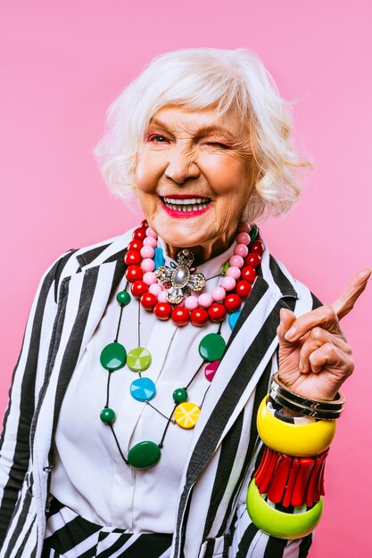 Porträt einer älteren Frau, die gegen einen rosa Hintergrund steht und Gesten macht