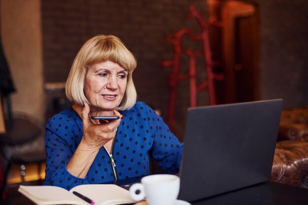 Porträt einer älteren Frau, die mit modernem Laptop drinnen im Café sitzt.