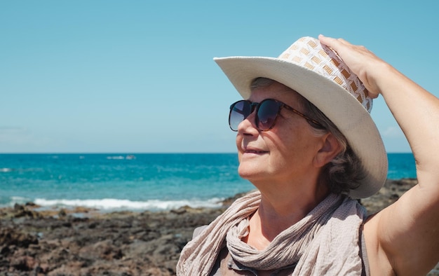 Porträt einer älteren Frau mit Hut und Sonnenbrille, die einen Seeurlaub am Strand genießt