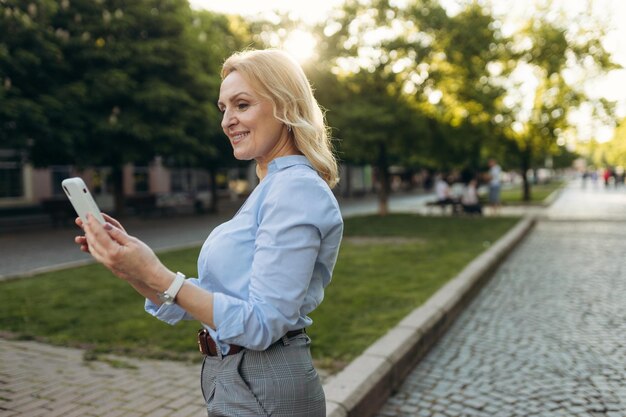 Porträt einer älteren Geschäftsfrau mit Smartphone in der Stadt Fröhliche, reife Geschäftsfrau in klassischer Kleidung