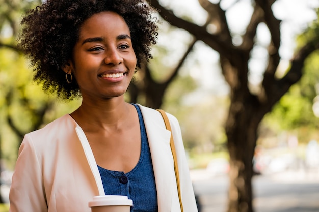 Porträt einer Afro-Geschäftsfrau, die lächelt und eine Tasse Kaffee hält, während sie draußen auf der Straße steht