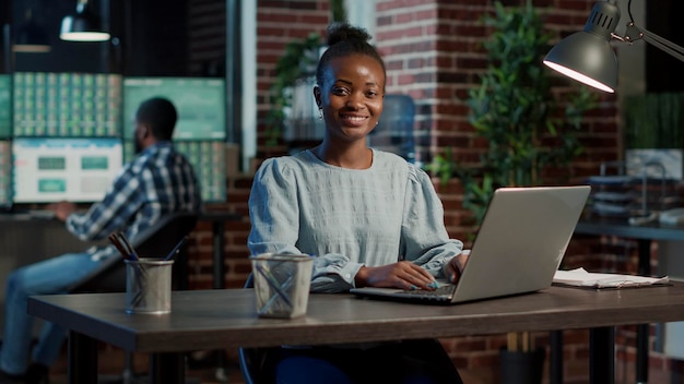 Porträt einer afroamerikanischen Frau, die mit Börsenstatistiken auf einem Laptop arbeitet und Devisenmarkthandelszahlen verwendet, um den finanziellen Gewinn zu analysieren. Investitionspreis für Hedgefonds.