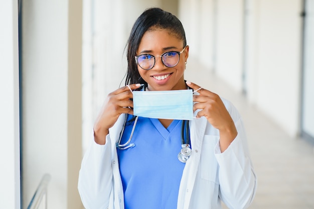 Porträt einer afroamerikanischen Ärztin mit Maske, die im Krankenhausflur steht. Medizin, Gesundheit und Gesundheitsdienste während der Coronavirus-Covid-19-Pandemie.