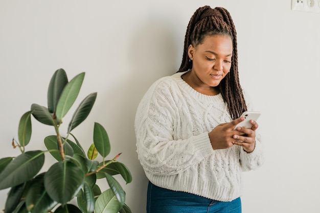 Porträt einer afroamerikanischen Studentin, die lässig gekleidet ist und ein Handy in der Hand hält, Nachrichten tippt und mit Freunden über soziale Netzwerke über eine hohe Internetverbindung kommuniziert