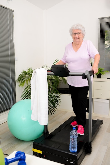 Porträt einer aktiven und dynamischen Seniorin, die zu Hause Sportfitness macht und auf dem Laufband geht