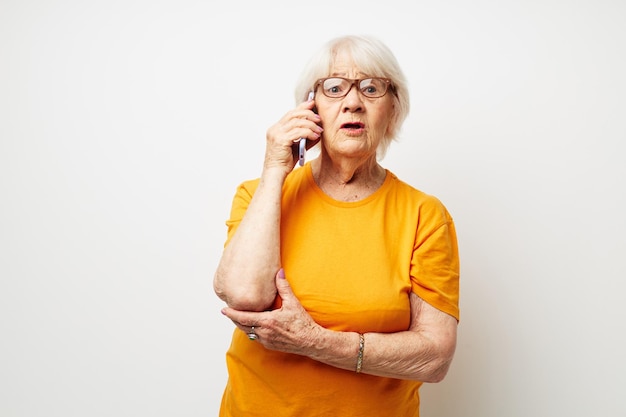 Porträt einer alten freundlichen Frau in einem gelben T-Shirt, das die Kommunikation per Telefon in der beschnittenen Ansicht darstellt