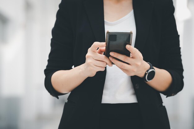 Porträt einer asiatischen berufstätigen Frau, die einen schwarzen Anzug trägt und ein Mobiltelefon hält