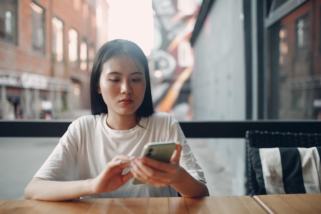 Porträt einer asiatischen Frau, die das Handy im Café im Freien genießt?