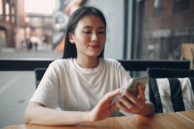 Porträt einer asiatischen Frau, die das Handy im Café im Freien genießt?