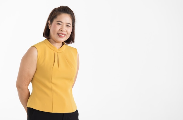 Porträt einer asiatischen Frau mittleren Alters, die eine gelbe Bluse trägt und schön mit selbstbewusstem isoliert lächelt.