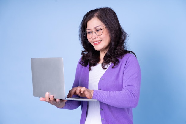 Porträt einer asiatischen Frau mittleren Alters mit Laptop auf blauem Hintergrund