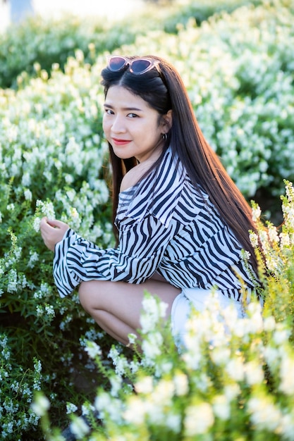 Porträt einer asiatischen jungen Frau, die einen glücklichen Reisenden mit schwarz-weißem Musterkleid genießt, das auf einem weiß blühenden Blumenfeld im Naturgarten von Thailandtravel Entspannungsurlaub genießt