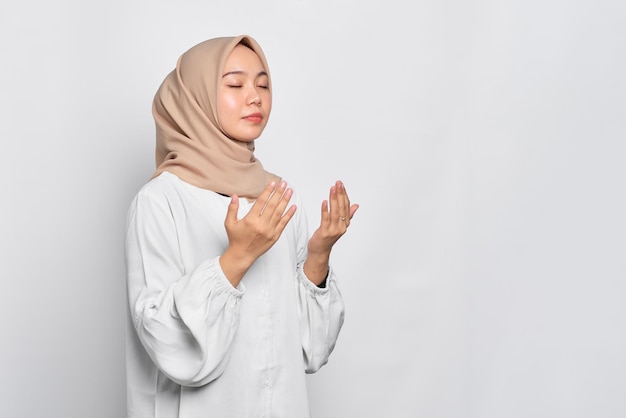 Porträt einer asiatischen muslimischen Frau, die mit offenem Arm betet, isoliert auf weißem Hintergrund
