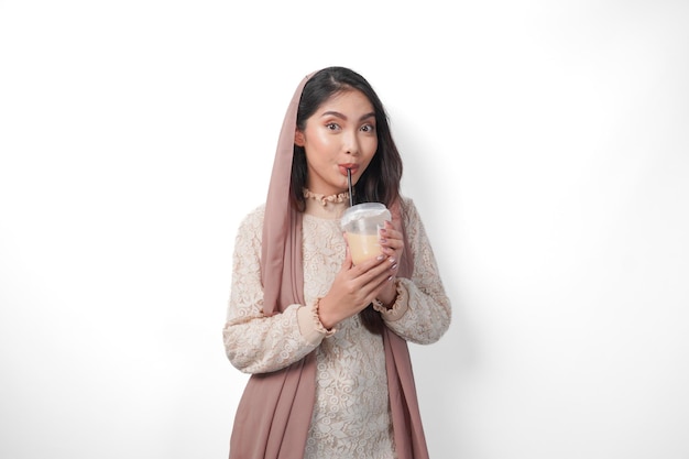 Porträt einer asiatischen muslimischen Frau mit Kopftuch, Schleier und Hijab, die nach dem Fasten Durst hat und Kaffee in einem Plastikbecher trinkt.