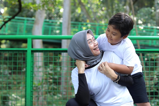 Porträt einer asiatischen muslimischen Mutter und eines Sohnes, die auf Augenhöhe schauen und die Zeit mit der Familie im Park genießen. Bondin